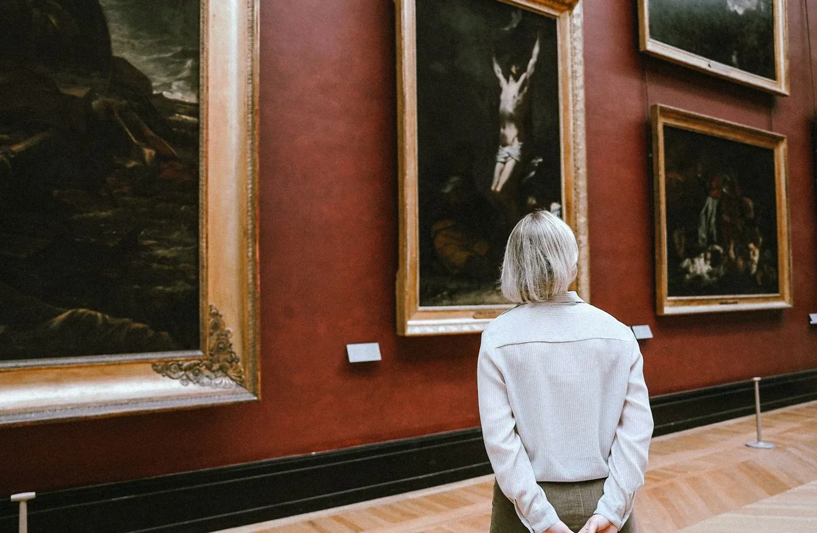 ギャラリーで額装された絵画を見上げる人の後ろ姿